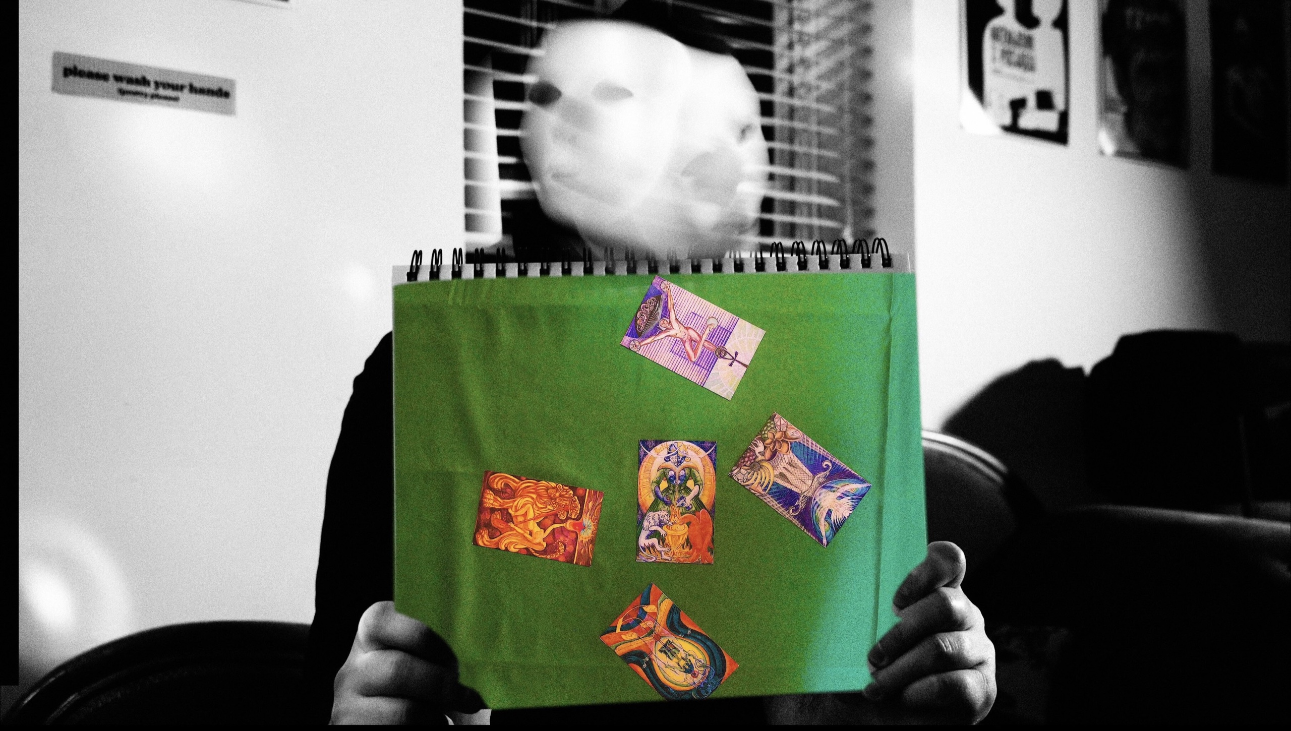 A masked figure holds a green book of tarot images in Moon in Scorpio.
