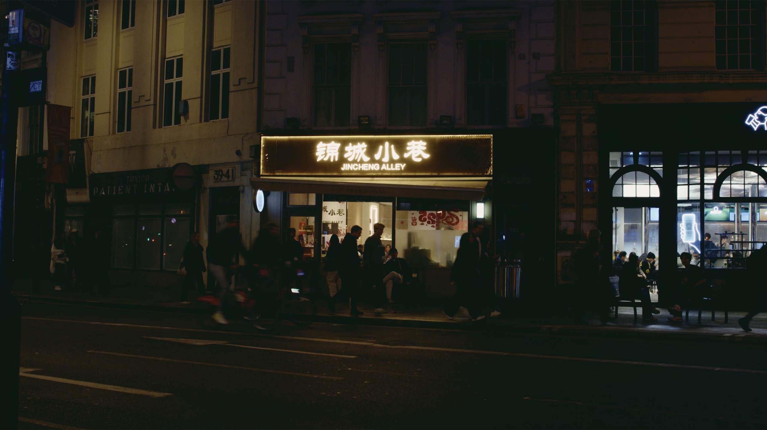 People moving past an illuminated storefront at night.