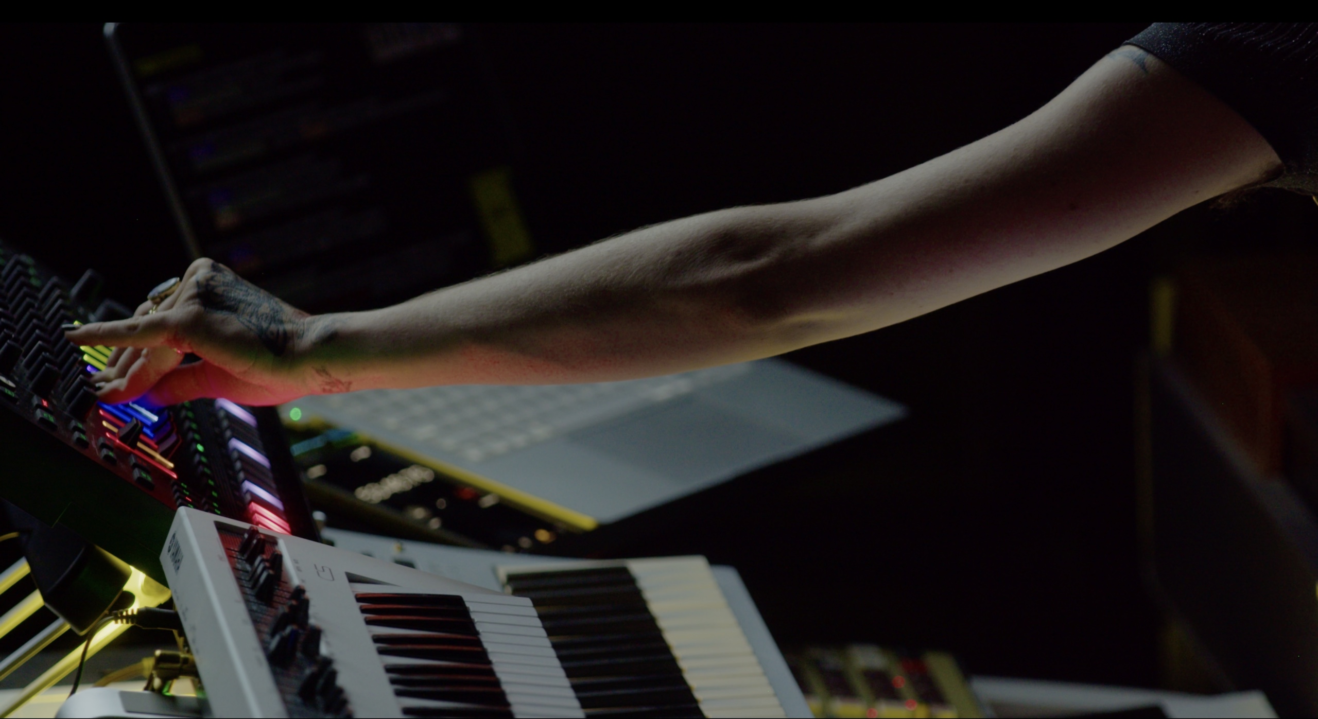 A musician reaching across illuminated synthesizer controls during a live film score.